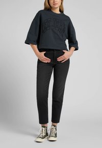 Dark grey cropped sweatshirt with "LEE JEANS" in bold print, paired with high-waisted black jeans and dark green high-top sneakers.