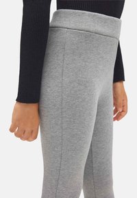 Leggings grises hechos de una tela suave, con una cinturilla alta y costuras laterales. Combinados con una blusa negra de manga larga acanalada.