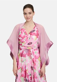 Lichtroze sjaal met satijnen randen gedragen over een bloemenjurk met een mix van roze, groen en paarse tinten in een gelaagd ontwerp.