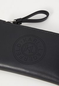Black leather pouch with a textured finish, featuring a perforated circular logo and a zip closure with a wrist strap.