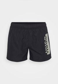 Shorts de bain noirs avec une taille élastique et un logo gris "HUGO" imprimé sur le côté gauche. Tissu léger et lisse, design à longueur de genoux.