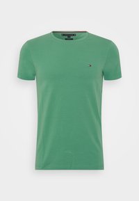 T-shirt vert à col rond et manches courtes avec un petit logo rouge, blanc et noir sur la poitrine gauche, design épuré.