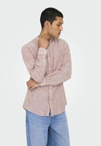 Camicia a maniche lunghe di un rosa chiaro realizzata in tessuto testurizzato, con bottoni sul davanti e colletto a fascia, abbinata a jeans in denim blu chiaro.