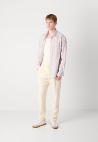 Camisa de rayas de manga larga en lavanda claro con un bolsillo en el pecho, combinada con pantalones de color crema y zapatillas blancas con detalles en beige.