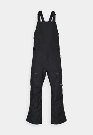 Salopette impermeabile nera per la neve con spallacci regolabili, multiple tasche con zip e vestibilità rilassata. Presenta aperture rinforzate sulle gambe.