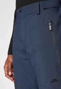 Marine tekniske bukser med en glat tekstur, glidelåslomme og logo detaljer. Har en klassisk passform og solid midjebånd.