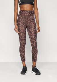 Κολάν ψηλόμεσα με καφέ σχέδιο λεοπάρ, κατασκευασμένο από ελαστικό ύφασμα, συνδυασμένο με μαύρα αθλητικά παπού τσια.