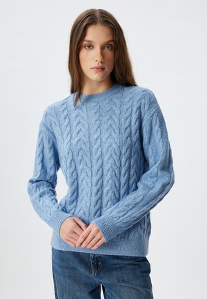 Lichtblauwe kabelgebreide trui met een ronde halslijn en geribbelde manchetten, gemaakt van zacht, textuurstof. Gecombineerd met denim jeans.