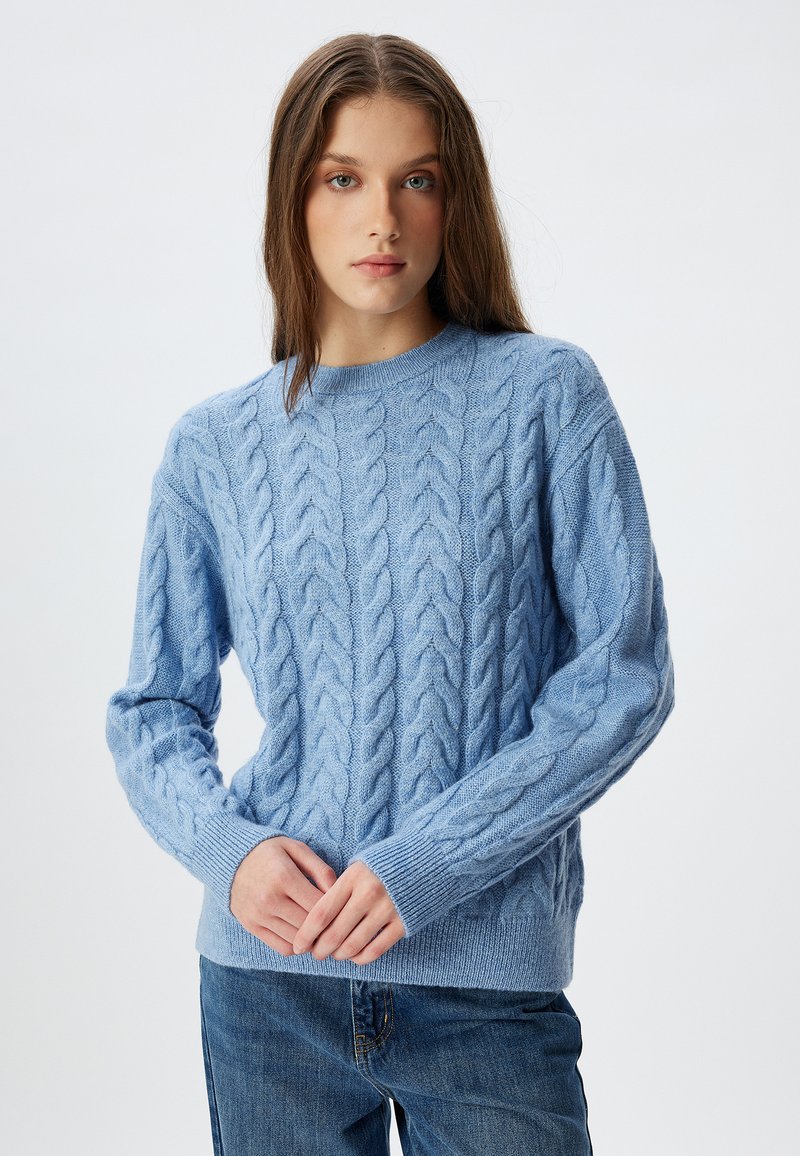 Maglioncino in maglia a treccia di colore azzurro chiaro, con scollo rotondo e polsini a costine, realizzato in morbido tessuto testurizzato. Abbinato a jeans di jeans.