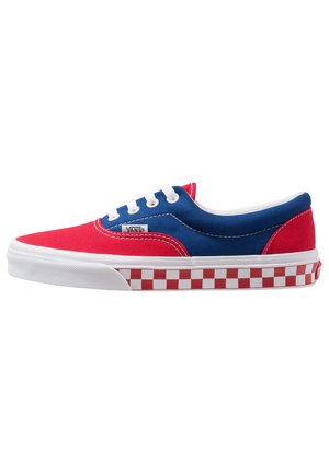 Red and blue canvas sneaker with white laces, featuring a red and white checkerboard pattern on the sole. Rounded toe and low profile design.