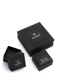 Boîtes d'emballage noires de différentes tailles, avec une texture mate et des étiquettes affichant le nom de la marque "Kuzzoi" ainsi que des informations sur le recyclage.