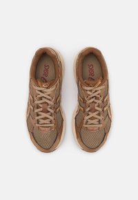 Sneaker in rete marroni con accenti più chiari, dotate di chiusura con lacci, linguetta imbottita, lati testurizzati e logo prominente sulla soletta.