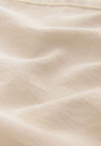 Tessuto beige chiaro con una trama fine e liscia e un sottile motivo a tessitura diagonale, che drappeggia delicatamente con pieghe e piegoline morbide.