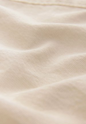 Šviesiai smėlio spalvos audinys su smulkia, lygiu tekstūra ir subtiliu įstrižainio pynimo raštu, švelniai krentantis su minkštais raukšlėmis ir prispaudimais.