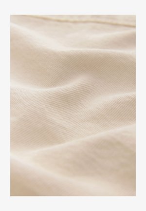 Šviesiai smėlio spalvos audinys su smulkia, lygiu tekstūra ir subtiliu įstrižainio pynimo raštu, švelniai krentantis su minkštais raukšlėmis ir prispaudimais.