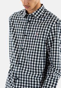 Zwart-wit geruite overhemd met lange mouwen, kraag en een klein logo op de borst. Katoenen materiaal met een soepele textuur.