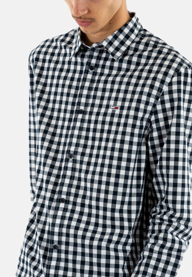 Zwart-wit geruite overhemd met lange mouwen, kraag en een klein logo op de borst. Katoenen materiaal met een soepele textuur.