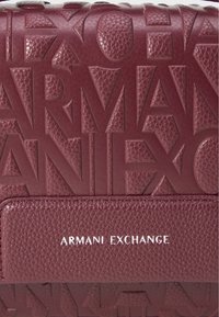 Geantă de piele maron, cu logo-ul embosat "ARMANI EXCHANGE", accente texturate și un panou orizontal neted cu branding alb.
