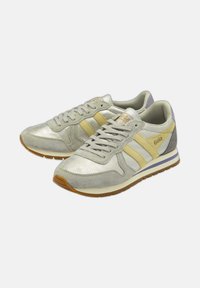 Sneaker grigie chiare con riflesso metallico, caratterizzate da strisce gialle e bianche, lacci rotondi e una suola in gomma marrone. Accentuate con un tallone grigio.