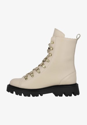 Bottine en cuir beige avec semelle épaisse noire à crampons, œillets dorés, lacets beiges et languette à l’arrière.