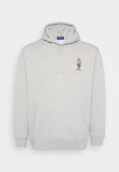 Sweatshirt capuz cinza claro com bolso frontal e pequeno urso bordado a usar um traje vintage acima do texto "Polo" no peito.