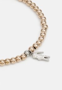 Bracelet en m étal avec des perles métalliques alternées en tons or et argent, agrémenté d'un pendentif argenté en forme de crocodile.