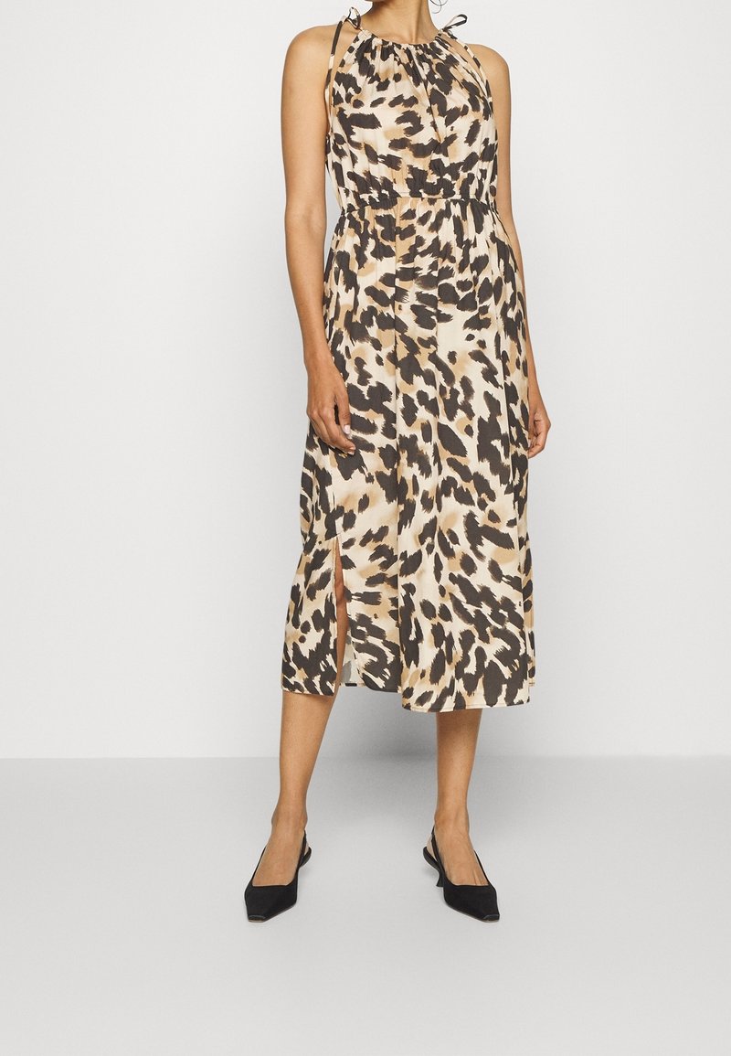 Leopardmönstrad midiklänning i beige och brunt, med halterneckskärning, elastisk midja och sidoklackar. Bärs tillsammans med svarta slingback-skor.