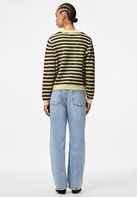 Striped sweater in dark brown and light yellow, made of soft material. Paired with wide-leg light blue jeans featuring rear pockets.