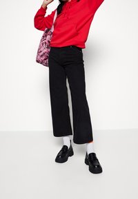 Röd hoodie med en framficka, svarta vida jeans, kraftiga svarta loafers och vita strumpor med en orange detalj. Rosa blommig tote-väska.