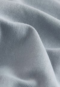 Hellgrauer Strickstoff mit feiner Rippenstruktur und weichen Falten, die sanfte Schatten und Lichtreflexe erzeugen.