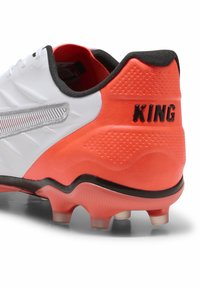 Talon de football blanc avec des accents noirs, un talon orange et des détails argentés. Présente une finition texturée et le mot "KING" affiché de manière proéminente.