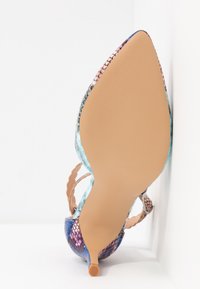 Chaussure à talon kitten à bout pointu avec motif multicolore en peau de serpent et bride de cheville, semelle tournée vers l'extérieur sur fond blanc.