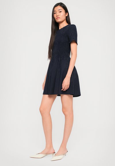 Tengerészek által viselt ruha rövid ujjakkal, textúrázott felsőrésszel és bővülő szoknyával. Diszkrét függőleges csíkokkal díszítve. Fehér, hegyes orrú mules cipővel párosítva.