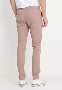 Beżowe spodnie slim fit wykonane z gładkiego materiału, z dwoma tylnymi kieszeniami, połączone z białymi sneakersami.