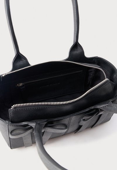 Μαύρη δερμάτινη τσάντα χειρός με ανοιχτό φερμουάρ στην κύρια θήκη και εσωτερική θήκη με φερμουάρ, διαθέτει διπλές λαβές και διακοσμητικά φιόγκους στο μπροστινό μέρος.