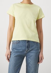 Gul bomullströja med korta ärmar och rund halsringning, i kombination med ljusblå denimjeans med rak skärning och synlig sömnad.