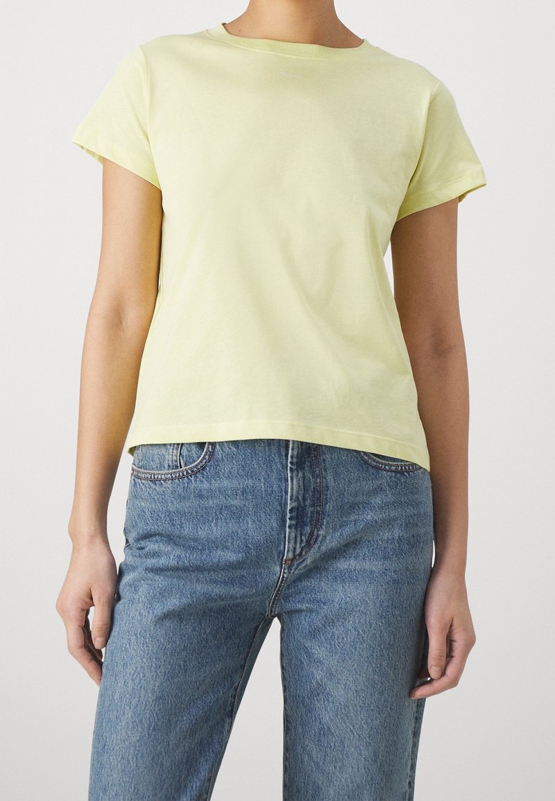 Gul bomullströja med korta ärmar och rund halsringning, i kombination med ljusblå denimjeans med rak skärning och synlig sömnad.