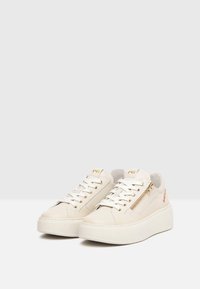 Zapatillas de plataforma blancas con una mezcla de materiales lisos y texturizados, con detalles de hardware dorado y una cremallera lateral.