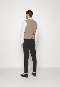 Ljust brunt väst med en slät yta, knäppning fram och justerbar baksida, kombinerad med svarta slim-fit byxor och svarta skor.