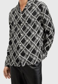 Camicia a maniche lunghe con bottoni in bianco e nero, caratterizzata da un motivo a quadri geometrici, realizzata in un tessuto morbido e dalla vestibilità rilassata. Due tasche frontali.