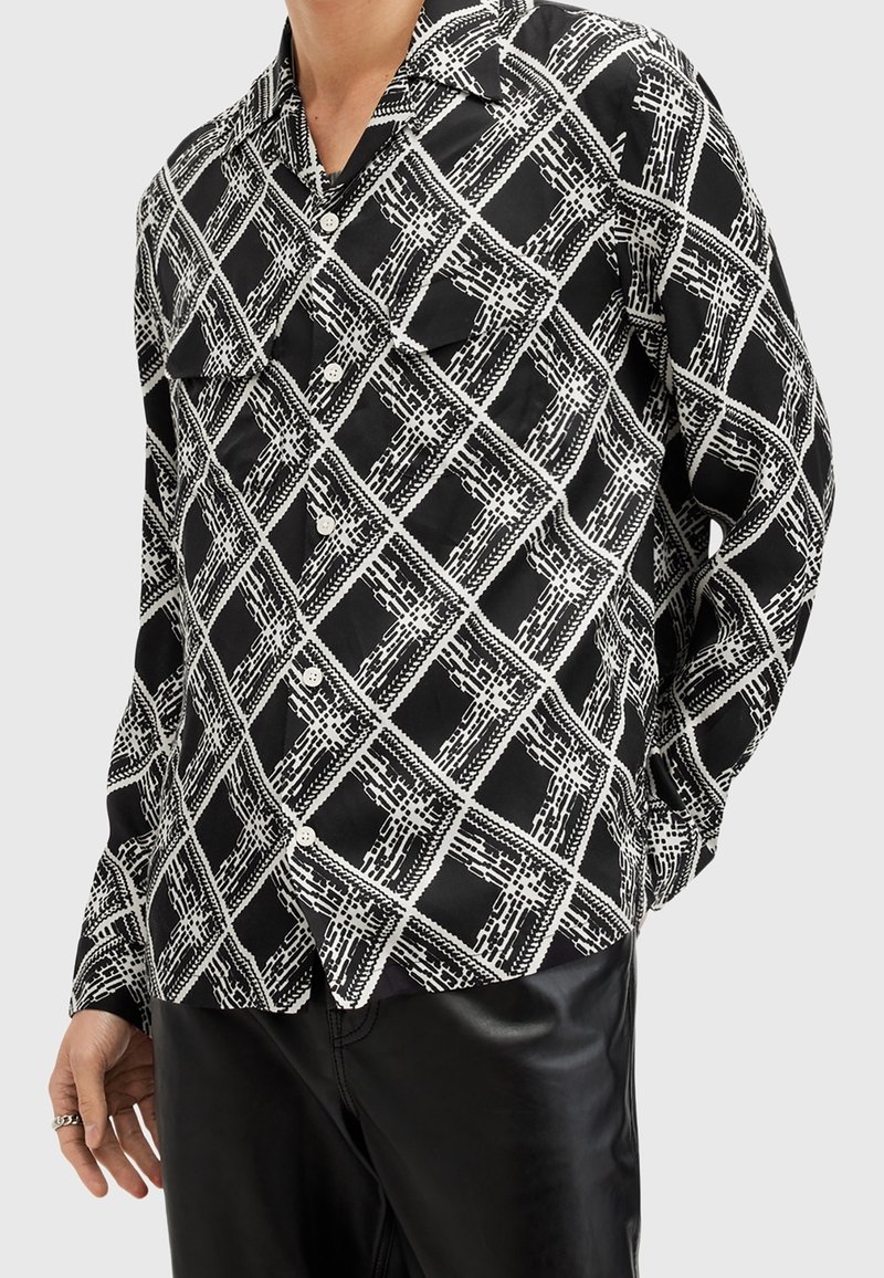 Camicia a maniche lunghe con bottoni in bianco e nero, caratterizzata da un motivo a quadri geometrici, realizzata in un tessuto morbido e dalla vestibilità rilassata. Due tasche frontali.
