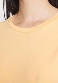 Koszulka na krótki rękaw, okrągły dekolt, wykonana z miękkiego żółtego materiału; gładka faktura z zaszytą dekoracją dekoltu. Idealna do codziennych stylizacji.