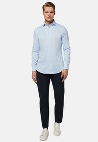 Svietlo modrá košeľa s dlhým rukávom vyrobená z hladkej tkaniny, s predným zapínaním na gombíky, klasickým golierom, v kombinácii s tmavými nohavicami a bielymi teniskami.