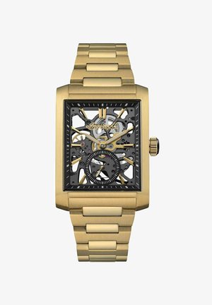 Orologio scheletrico rettangolare con finitura dorata, quadrante nero, ingranaggi visibili e dettagli neri. Bracciale in metallo con design a maglie e superficie texturizzata.