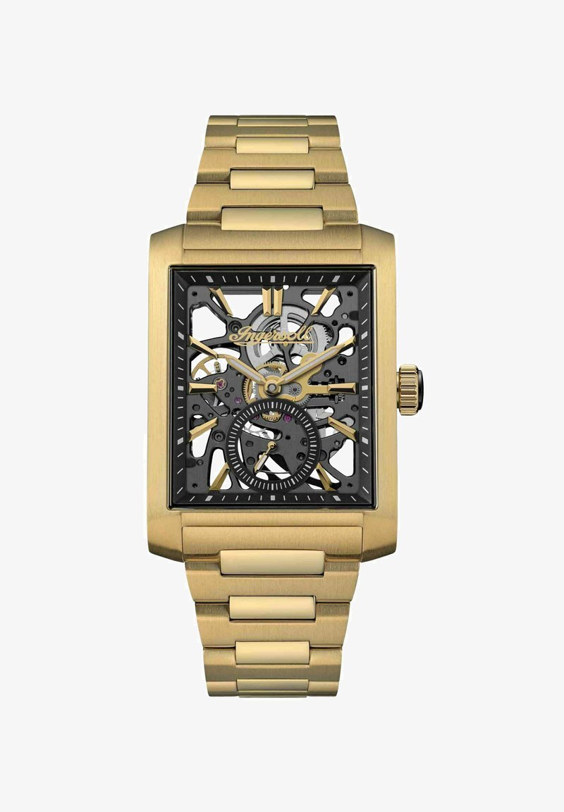 Złoty prostokątny szkieletowy zegarek z czarną tarczą, widocznymi mechanizmami i czarnymi akcentami. Metalowa bransoleta o połączonej konstrukcji i teksturowanej powierzchni.
