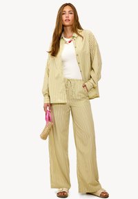 Conjunto a rayas en verde claro y beige que incluye una camisa holgada de botones y pantalones de pierna ancha. Los accesorios incluyen una pequeña bolsa de mimbre y sandalias.