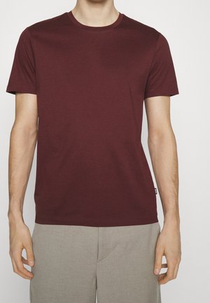 Bordeauxrotes T-Shirt mit Rundhalsausschnitt aus Baumwolle, mit kurzen Ärmeln und einer glatten, gleichmäßigen Textur sowie einem Etikett auf der linken Seite.