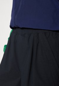 Maglia con zip di colore navy abbinata a una gonna nera con texture; la gonna presenta una fascia elastica in vita e un tessuto morbido e plissè con sottili strisce.