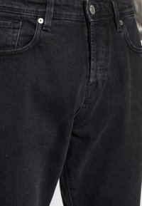 Svarta jeans i denim med klassisk skärning, med ton-i-ton-sömmar, framfickor och metallknapp. Tyget har en lätt struktur.