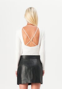 White long-sleeve top with a deep V-cut back and crisscross straps, paired with a black leather mini skirt, smooth texture, and fitted design.